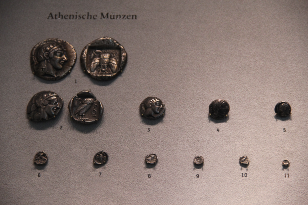 Eine Sammlung von antiken Münzen in verschiedenen Formen und Größen, die in einem Museum ausgestellt sind, mit Text auf ihren Oberflächen.