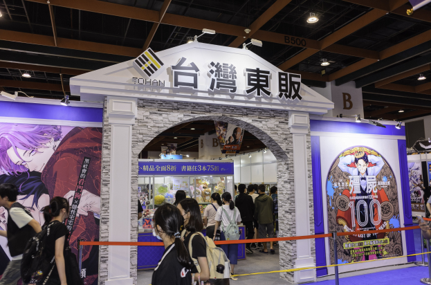 Gruppe von Menschen vor einer Spielshow-Bühne auf einer Messe, mit Werbetafeln und Deckenbeleuchtung.