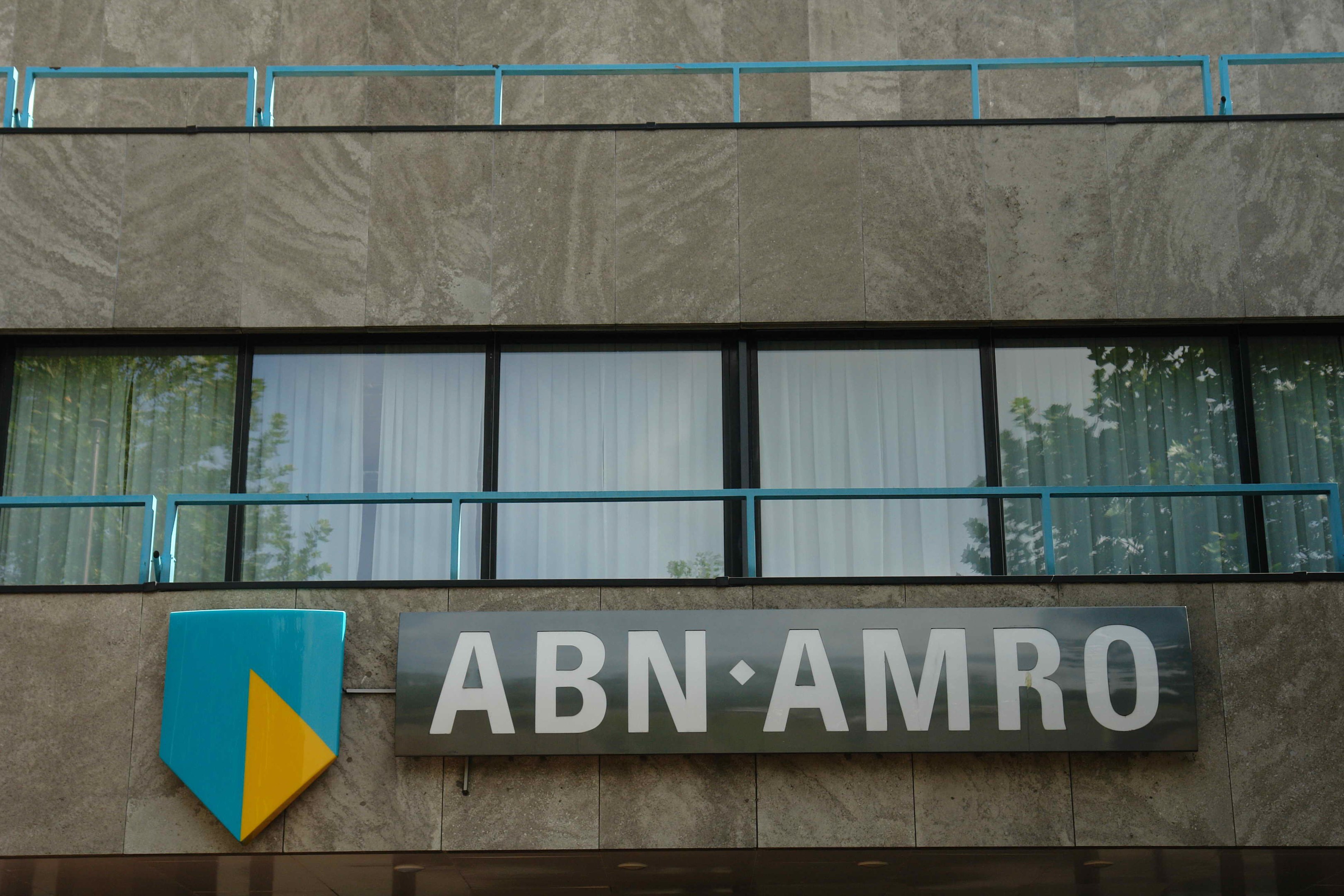 Gebäudefassade mit "ABN AMRO"-Schriftzug, eine Tafel, die es als Unternehmenshauptsitz angibt, Geländer und Vorhänge an Glasfenstern.