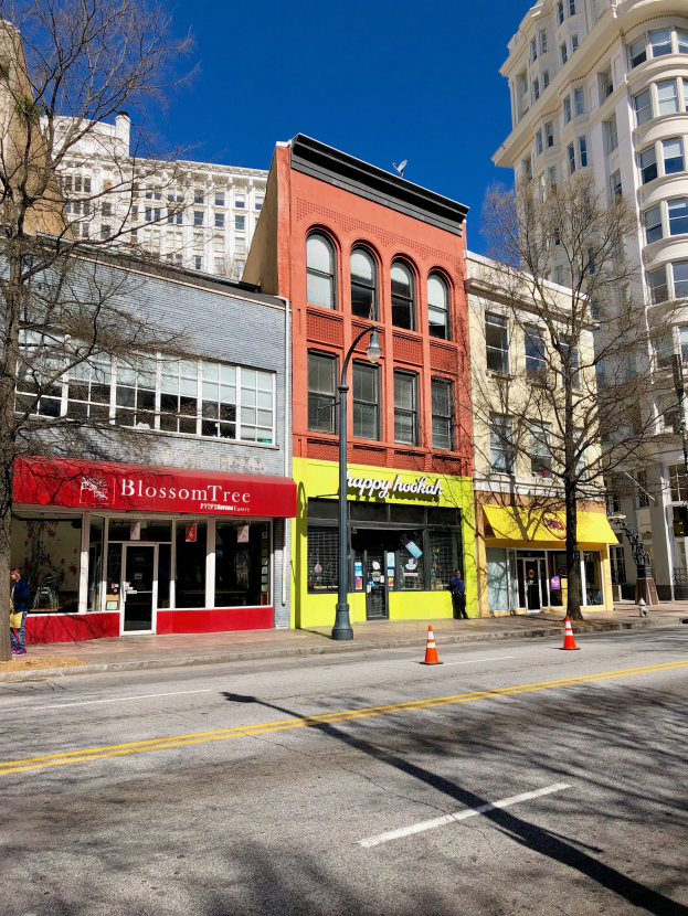 Eine Stadtstraße in Portland mit hohen Gebäuden auf beiden Seiten, Straßenlaternen, Verkehrsschildern, Autos, Fußgängern auf dem Gehweg, Bäumen und einem bewölkten Himmel.