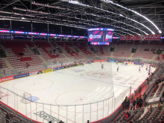 Ein Hockey-Spiel in einer großen Arena mit Zuschauern auf Sitzplätzen und Stehplätzen, einem Zaun um die Eisfläche, einem Display mit der Aufschrift "St. Louis Blues vs Detroit Red Wings", Metallrahmen und einer Decke mit Leuchten.