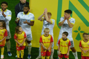 Eine Gruppe von Fußballspielern in Uniformen, die auf einem Feld mit einem "Ligue 1"-Schild im Hintergrund klatschen, feiern einen Sieg.