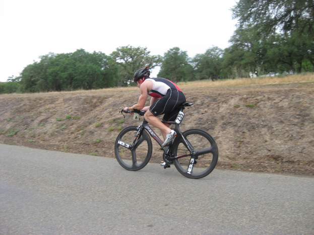 Eine Person mit Helm fährt ein Fahrrad mit Bäumen und Gras im Hintergrund.