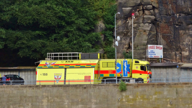 Ein Rettungswagen steht auf der Seite einer Straße neben einer Klippe, mit verschiedenen Gegenständen im Vordergrund und Bäumen und einem Auto im Hintergrund.