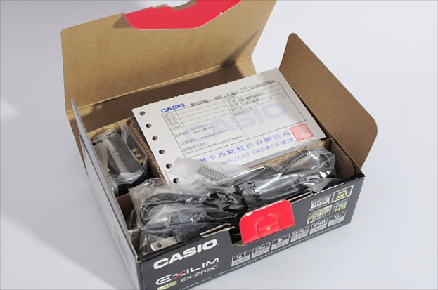 Ein Casio-Kasten auf einer weißen Oberfläche, offen, um innere Drähte und eine Quittung zu enthüllen.