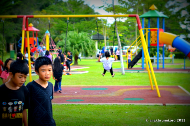 Kinder auf Spielgeräten in einem Park mit Bäumen.
