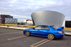Ein blaues Auto fährt auf einer Straße mit Gebäuden im Hintergrund.