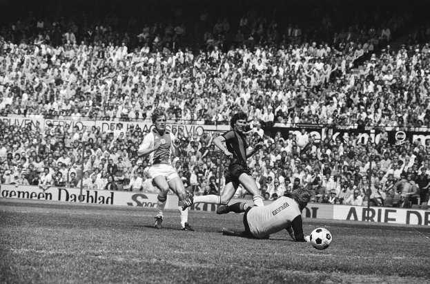 Schwarzes und weißes Foto von Männern, die auf einem Feld Fußball spielen, mit Zuschauern im Hintergrund und einer "Bundesliga 1978-79 Ajax 1-1 Hannover 96"-Aufschrift.