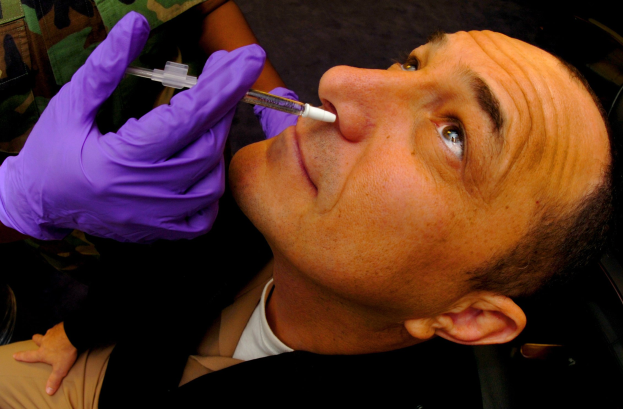 Ein Arzt in lila Handschuhen spritzt einem Mann mit einer Spritze ein Vakzin in den Mund.