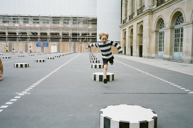 Ein Spielplatz mit vier Kindern, eines laufend auf einem schwarzen und weißen Zementstufenbereich, umgeben von einem Schulgebäude.