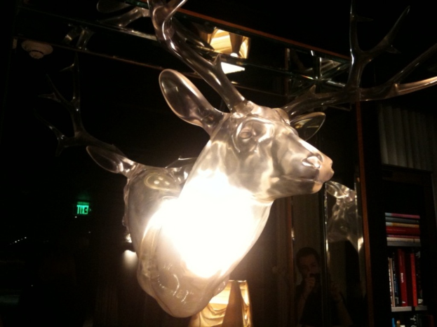 Eine Hirschstatue steht in einem Gebäude, mit einem Bücherregal rechts daneben.