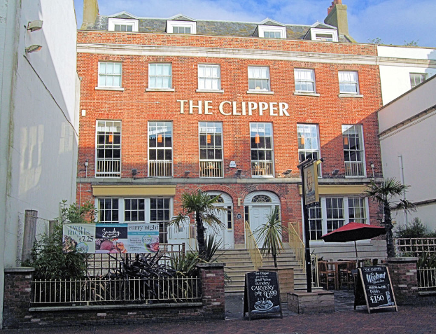 Ein Restaurant mit mehreren Fenstern und zwei Türen, umgeben von Bäumen, Brettern und einem weißen Zaun.