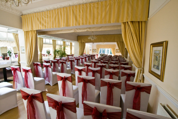 Ein Blick in den Innenraum eines Saals mit Sitzreihen, einem Vorhang, einem Holzrahmen, Topfpflanzen und einer Wand.