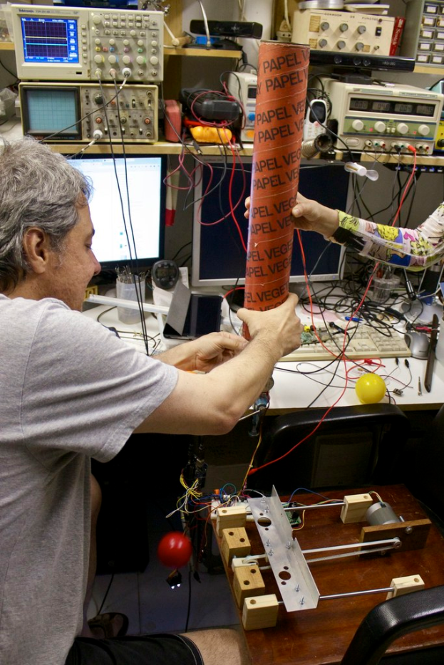 Ein Arbeitsplatz mit Maschinen, Kabeln, einem Computerbildschirm, einem Stiftbehälter, Menschen und einem Stressball.