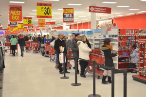 Ein volles Walmart-Geschäft mit Einkaufstägern mit Taschen und Einkaufswagen, umgeben von Warenregalen, Informationsschildern und Deckenleuchten, wahrscheinlich während eines Black Friday-Verkaufs.