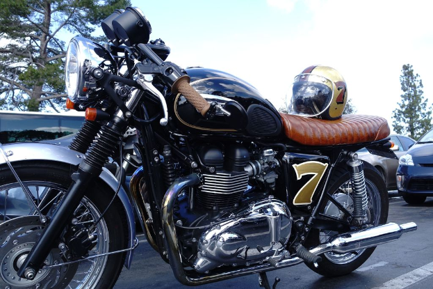 Ein Fahrrad mit Helm darauf befindet sich in der Mitte des Bildes, mit Autos, Bäumen und Himmel im Hintergrund und einer Straße unten.