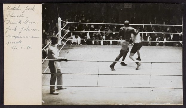 Schwarzes und weißes Foto von zwei Boxern im Ring mit einem Schiedsrichter links und Zuschauern im Hintergrund, betitelt mit "Jack Johnson vs Frank Morgan".