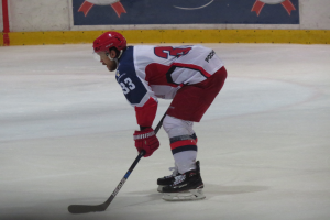 Hockeyspieler in voller Ausrüstung auf dem Eis mit einem Banner mit Text und Logos im Hintergrund.