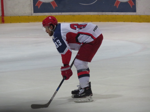 Hockeyspieler in voller Ausrüstung auf dem Eis mit einem Banner mit Text und Logos im Hintergrund.