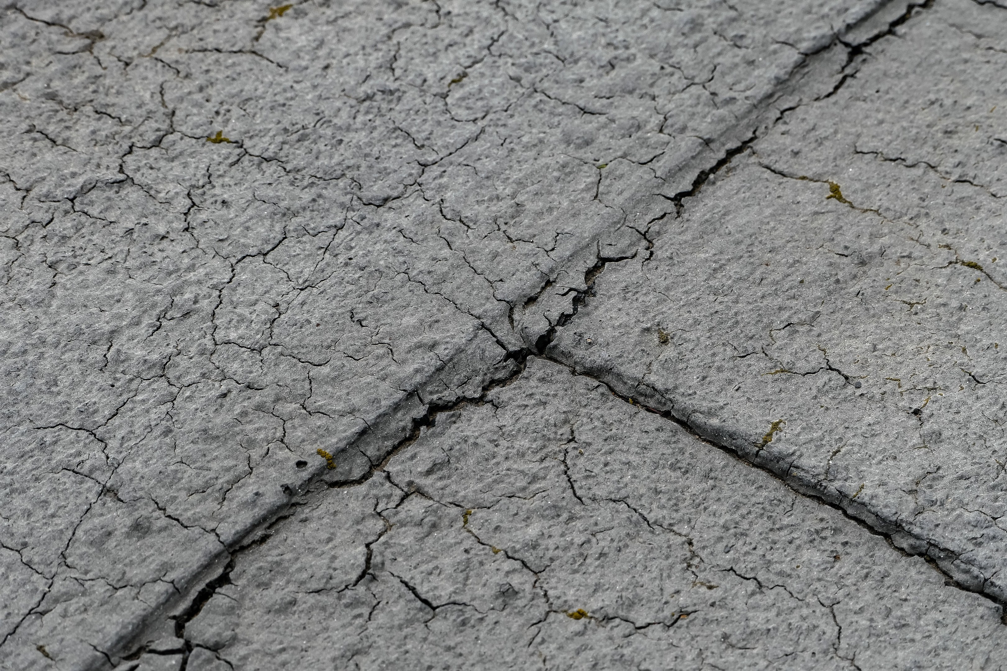Nahaufnahme einer gebrochenen, wettergegerbten Straßenoberfläche mit tiefen, breiten Rissen und rauer, unebener Textur.