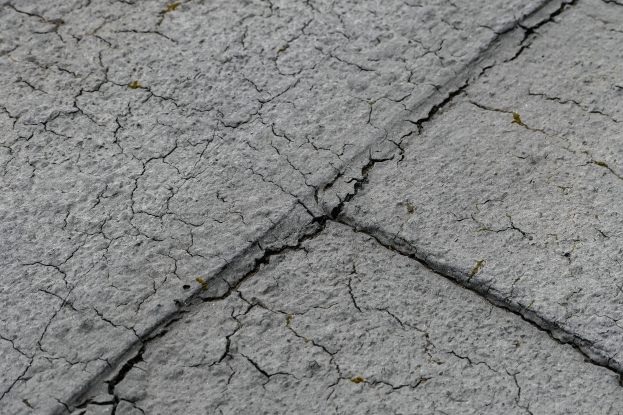 Nahaufnahme einer gebrochenen, wettergegerbten Straßenoberfläche mit tiefen, breiten Rissen und rauer, unebener Textur.