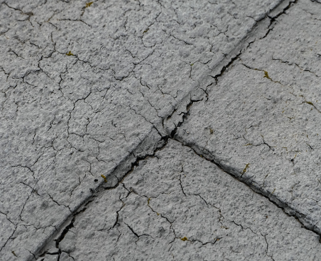 Nahaufnahme einer gebrochenen, wettergegerbten Straßenoberfläche mit tiefen, breiten Rissen und rauer, unebener Textur.