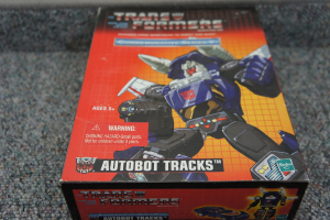 Ein roter, oranger und blauer Kasten mit einem Roboter oben drauf und dem Text "AUTOBOT TRACKS" vor einem unscharfen schwarzen Hintergrund.