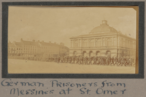 Deutsche Kriegsgefangene aus Messines vor einem Gebäude mit einem klaren blauen Himmel im Hintergrund, Text unten.