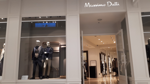 Innenansicht des Massimo Dutti Geschäftes in Mailand, Italien, mit Schaufensterpuppen in moderner Kleidung, beleuchteter Decke, Informationsschildern und sichtbarem Boden.