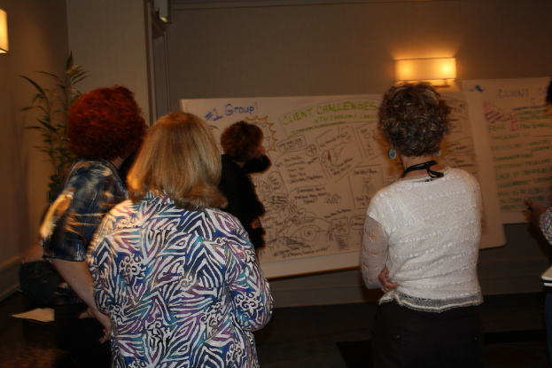 Viele Frauen vor einer wei├čen Tafel mit Text darunter einer an der Wand montierten Lampe, mit einer Pflanze auf der linken Seite, in einem Raum.