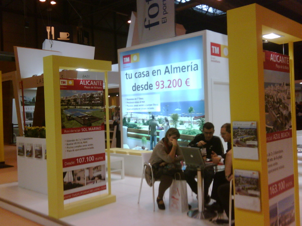 Eine Gruppe von Menschen sitzt um einen Tisch und schaut auf einen Laptop, mit mehreren Flyern, die verschiedene Werbeanzeigen zeigen.