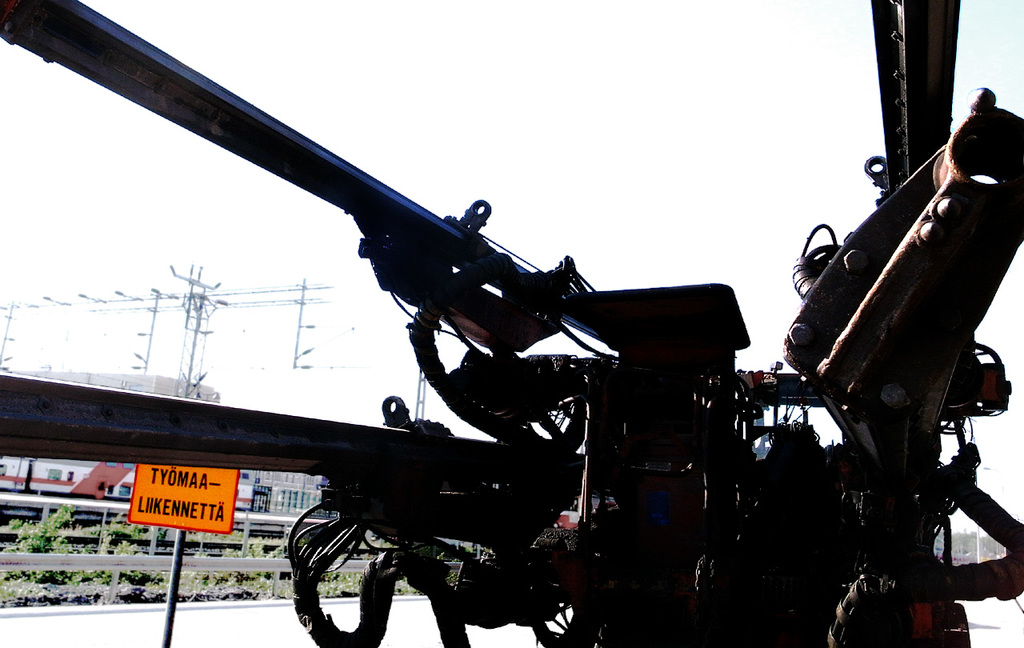 Eine Maschine vorne mit Strommasten, Kabeln, Absperrungen, Pflanzen und Himmel im Hintergrund.