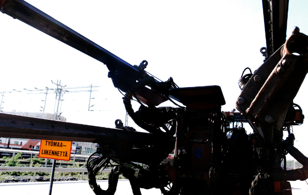 Eine Maschine vorne mit Strommasten, Kabeln, Absperrungen, Pflanzen und Himmel im Hintergrund.