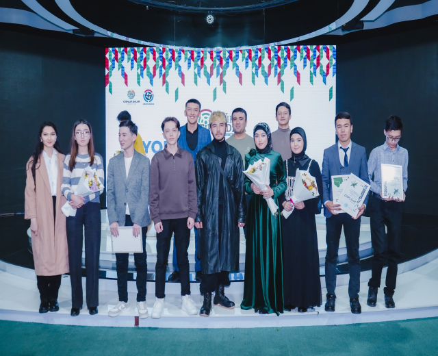 Gruppe von Menschen auf einer Bühne mit Blumensträußen und Urkunden, mit einem "Jugend-Solar-Awards 2019"-Plakat im Hintergrund.