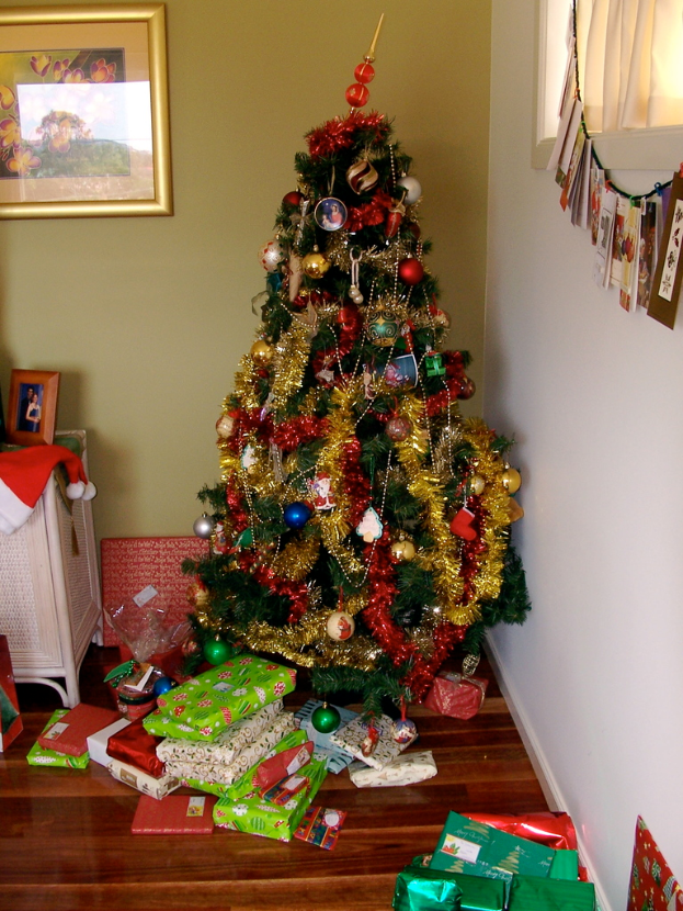 Ein geschmückter Weihnachtsbaum auf der rechten Seite mit Geschenken am Boden, ein Foto Rahmen an der linken Wand und ein Vorhang am rechten Fenster.