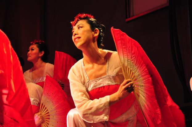 Eine Gruppe von Menschen mit Fächern in der Hand, mit einem gerahmten Bild im Hintergrund.