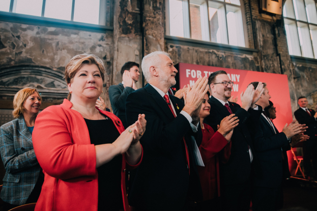 Eine Gruppe von Menschen steht vor einer Menge und klatscht, mit einem Banner im Hintergrund.