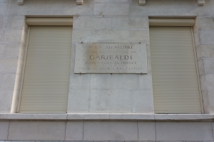 Ein Gebäude mit zwei Fenstern und Läden sowie einer Gedenktafel an der Seite.