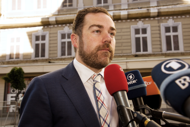 Ein Mann im Anzug spricht an einem Podium mit Mikrofonen vor einem Gebäude, wahrscheinlich spricht er mit der Medien nach einer drei-jährigen Haftstrafe.