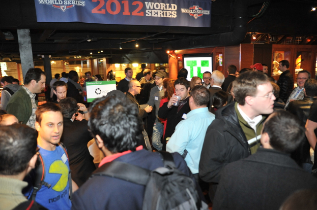 Große Menschenmenge bei einem Event mit einem Bildschirm, Lichtern und einer Holzwand im Hintergrund.