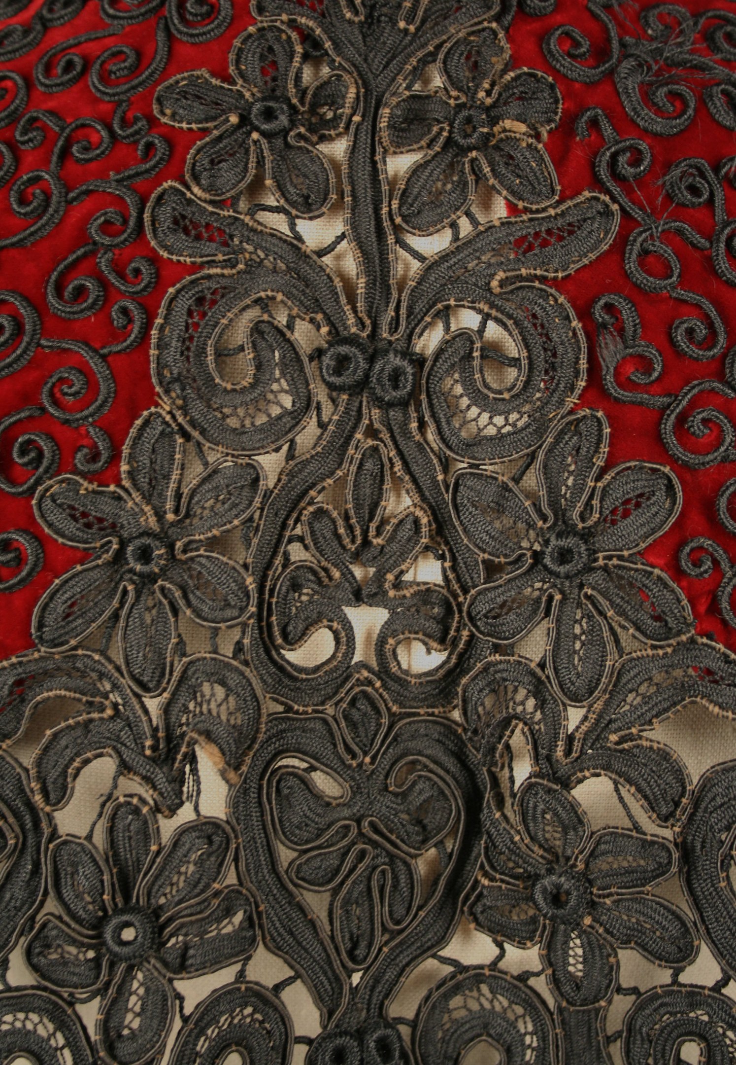 Nahaufnahme eines roten Kleides mit schwarzer Spitzenüberlagerung, das detaillierte Spitzenmuster auf dem roten Stoff zeigt.