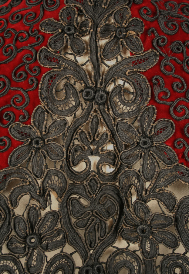 Nahaufnahme eines roten Kleides mit schwarzer Spitzenüberlagerung, das detaillierte Spitzenmuster auf dem roten Stoff zeigt.