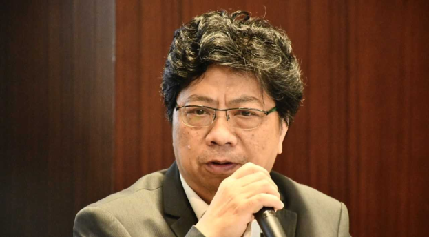 Mann in Anzug und Krawatte mit Mikrofon vor einem Holzwandhintergrund