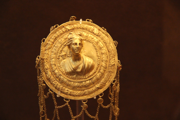 Goldene Medaille mit einer Frauengestalt auf dunklem Hintergrund, mit feiner Verzierung und königlich anmutendem Aussehen.
