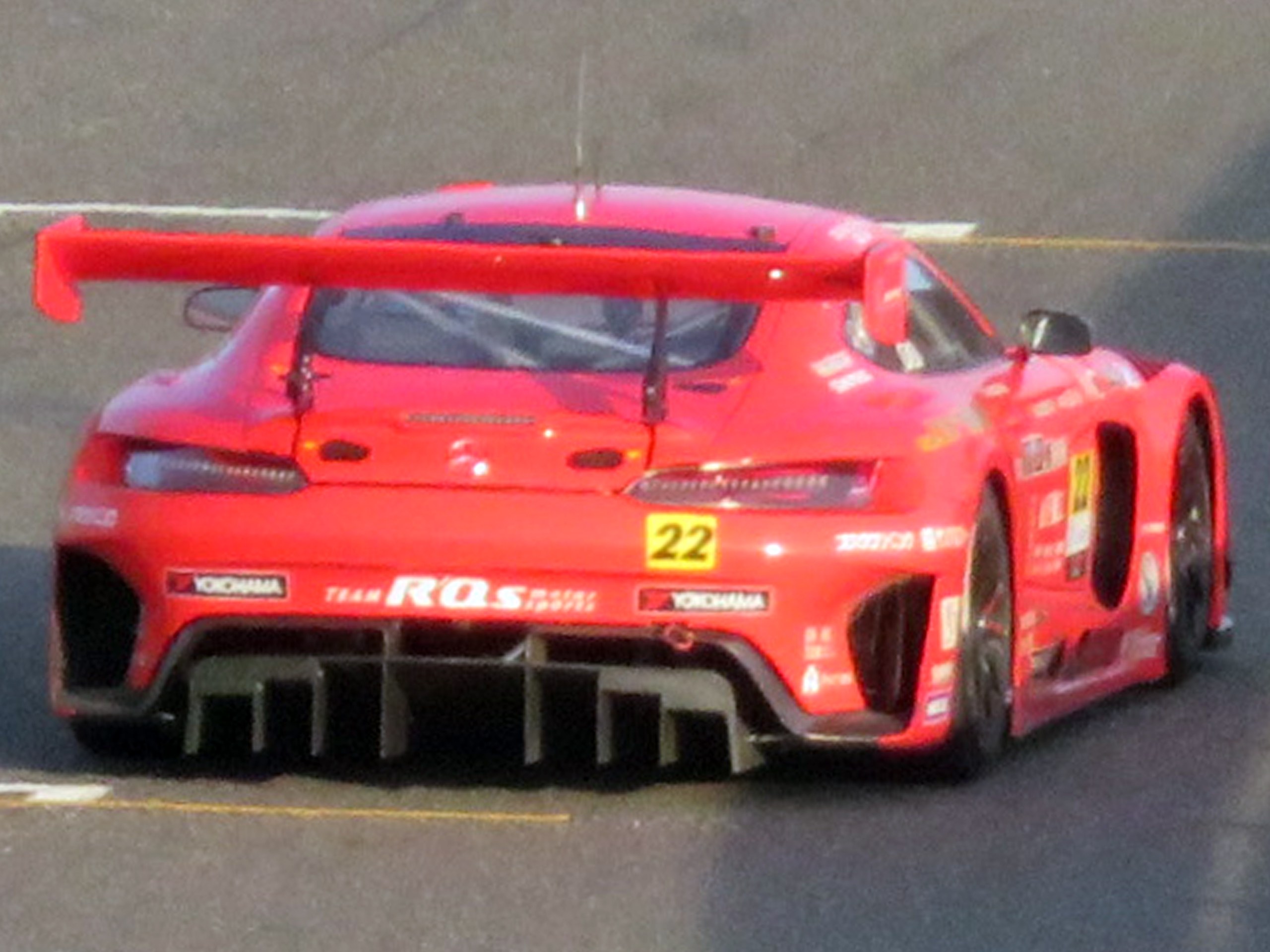 Roter Porsche 911 GTS Rennauto auf einer Rennstrecke mit aerodynamischem Design, großem Heckspoiler, breiter stance und schwarzen Rädern.