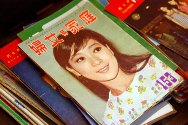 Eine Sammlung von Zeitschriften auf einem Tisch, wobei die vorderste Zeitschrift ein Bild einer Frau zeigt.