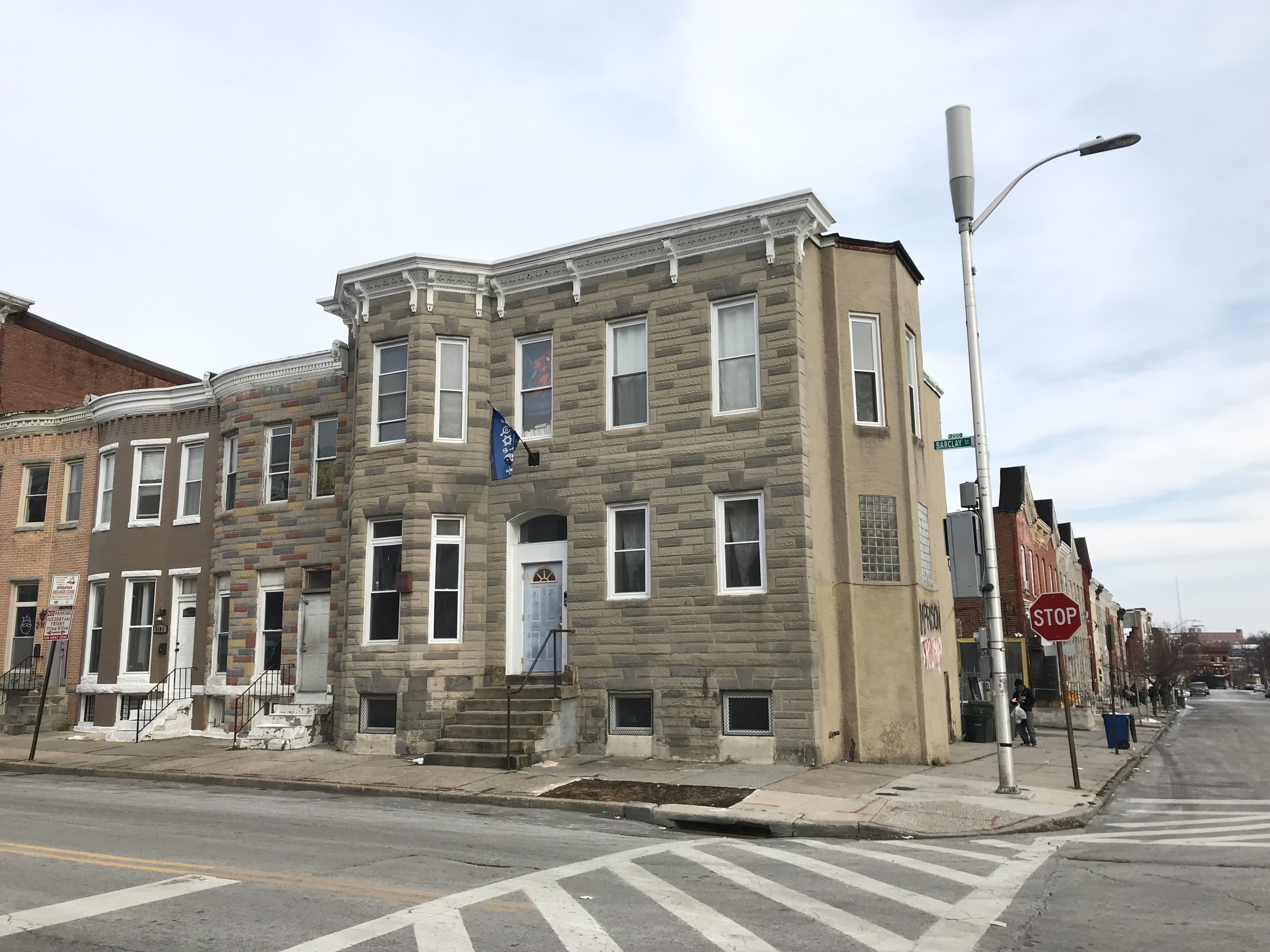 Eine Reihe moderner Häuser an einer Straßenecke mit Fahrzeugen, Bäumen und einem bewölkten Himmel im Hintergrund.