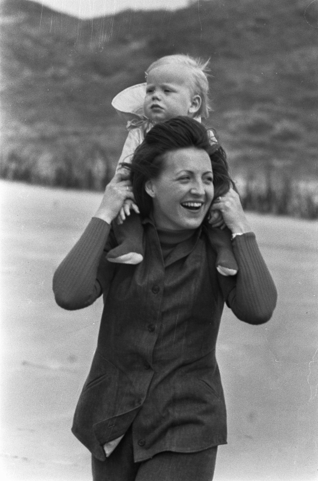 Eine Frau mit warmem Lächeln, die ein Baby hält, vor einem leicht unscharfen Hintergrund