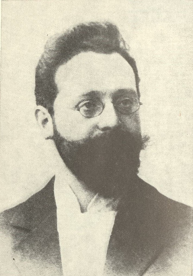 Schwarz-weiß-Porträt eines bärtigen Mannes in Anzug und Krawatte mit ernstem Gesichtsausdruck, konzentriertem Blick und ordentlich frisiertem Haar und Bart.