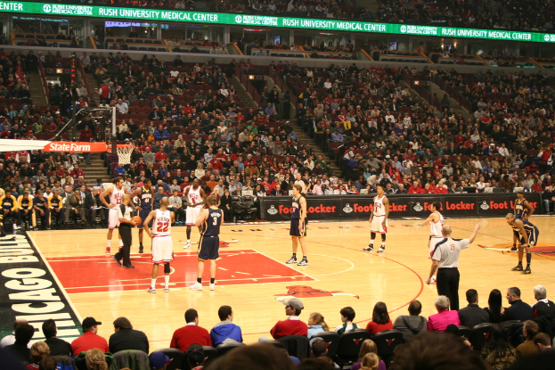 Eine Gruppe von Menschen in einem Stadion, einige halten einen Basketball, andere schauen von den Rängen und Werbetafeln sind auf den Planken zu sehen.